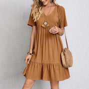 Abito estivo donna marrone, maniche corte, scollo a V, tessuto leggero, borsa a tracolla in paglia, moda casual, look estivo elegante.