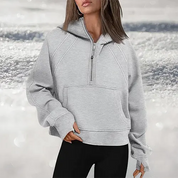 Donna con felpa grigia con cappuccio e zip, sfondo innevato. Abbigliamento casual invernale, moda donna, felpa comoda e calda.