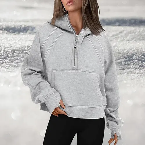 Donna con felpa grigia con cappuccio e zip, sfondo innevato. Abbigliamento casual invernale, moda donna, felpa comoda e calda.