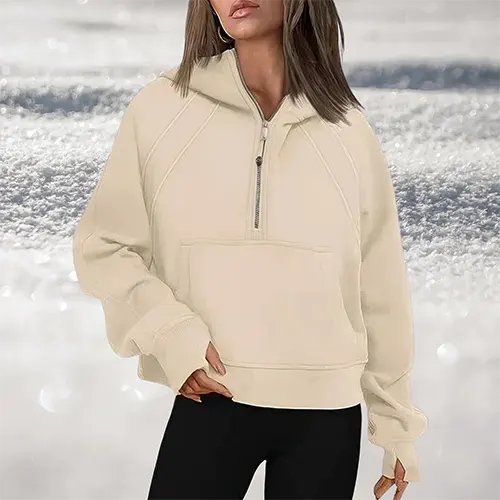 Felpa beige con cappuccio e zip, indossata da una donna su sfondo innevato. Moda invernale, abbigliamento casual, stile comodo e caldo.
