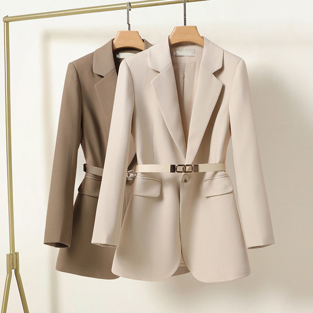 Due blazer eleganti da donna, beige e marrone, appesi su grucce. Design moderno con cintura in vita. Abbigliamento formale, moda femminile.