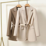 Due blazer eleganti da donna, beige e marrone, appesi su grucce. Design moderno con cintura in vita. Abbigliamento formale, moda femminile.