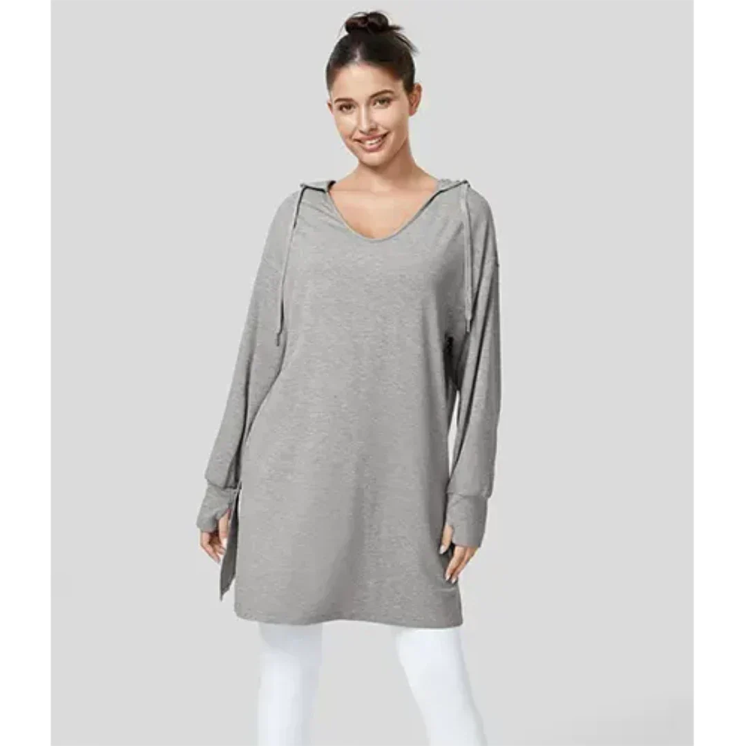 Donna con felpa oversize grigia con cappuccio, maniche lunghe, su sfondo grigio. Moda casual, abbigliamento comodo, stile autunnale.