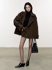 Donna con cappotto marrone oversize, maglione nero, shorts marroni, collant trasparenti, borsa nera e mocassini neri. Moda autunnale elegante.