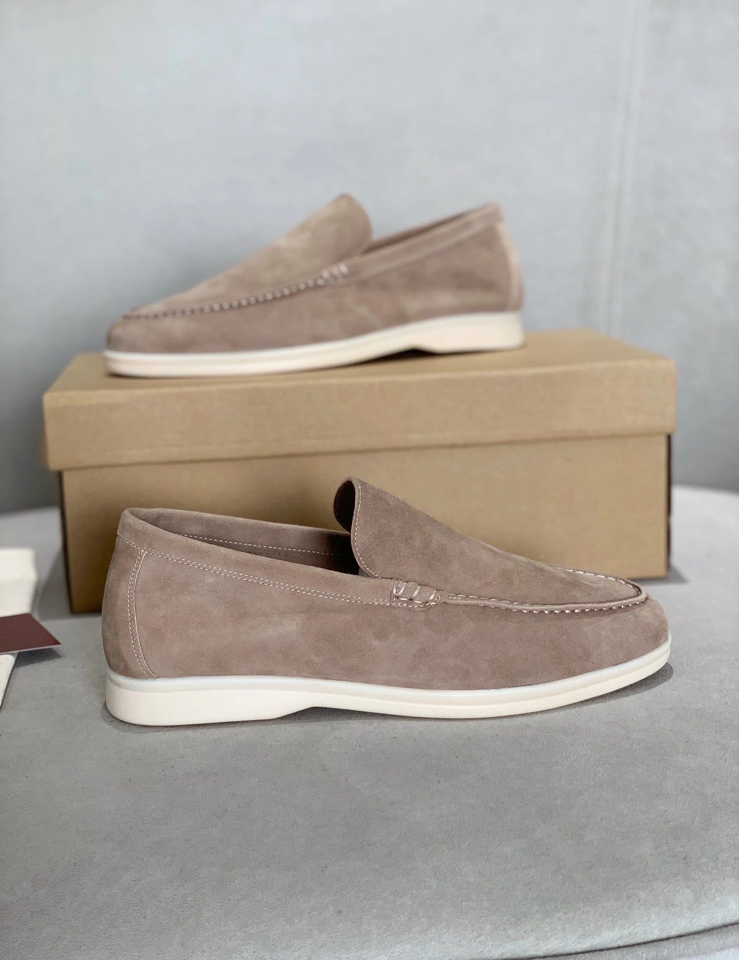 Mocassini in pelle scamosciata beige su scatola di cartone, design elegante e casual, perfetti per moda uomo, calzature di alta qualità.