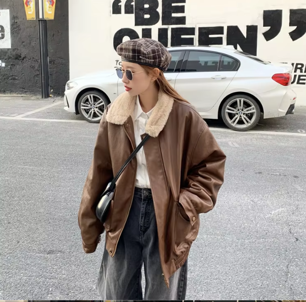 Giacca di pelle marrone con colletto in pelliccia sintetica, indossata da una persona in strada. Moda urbana, stile casual, cappello a quadri.