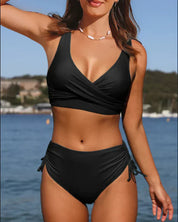 Donna in bikini nero a vita alta, top incrociato, collana bianca, sfondo marino. Costume da bagno elegante, moda estiva, spiaggia.
