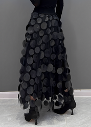 Gonna lunga nera con cerchi decorativi, design elegante e moderno, indossata con stivali neri su sfondo grigio. Moda femminile autunno inverno.