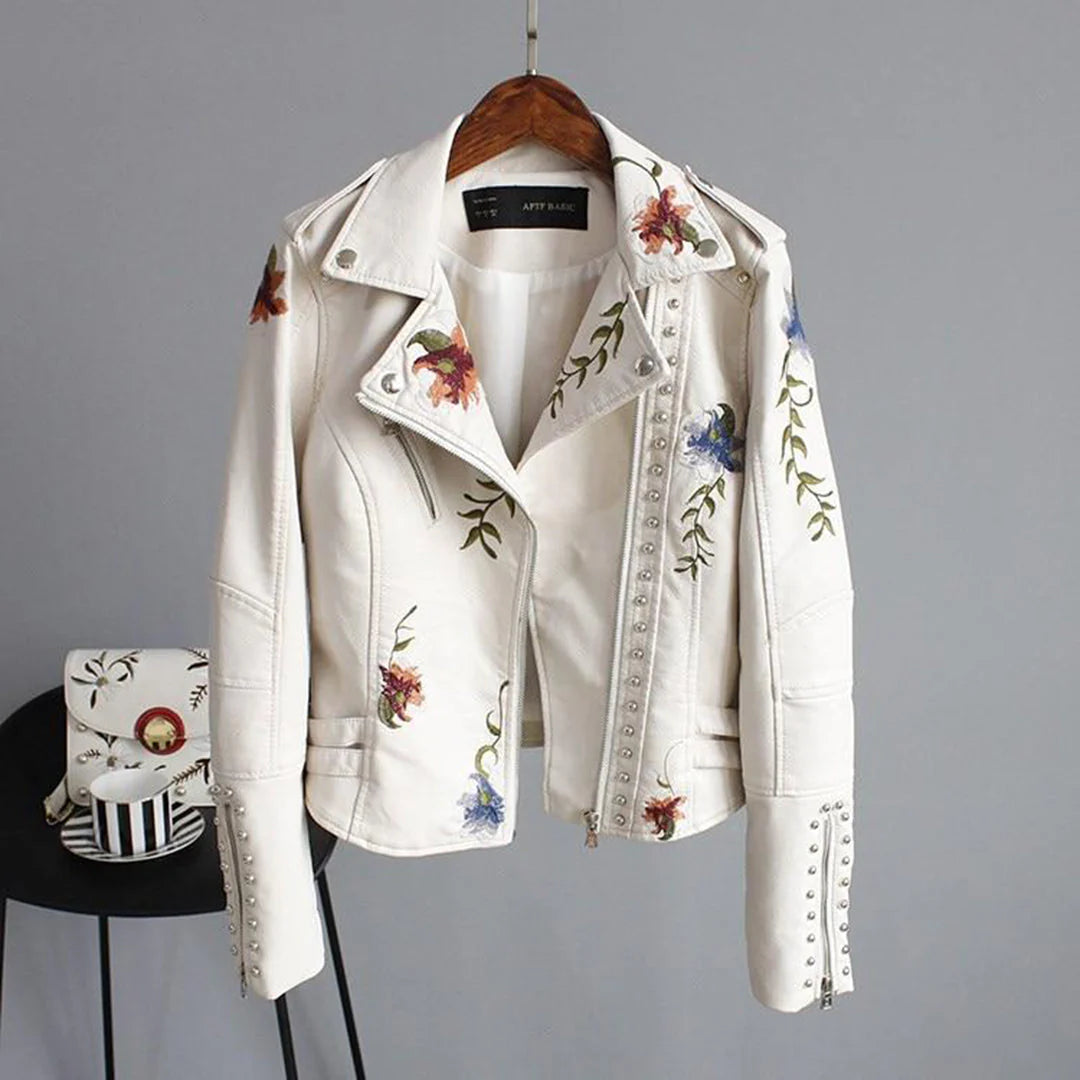 Giacca biker bianca in pelle con ricami floreali colorati, borchie decorative e zip, appesa su gruccia. Moda donna, abbigliamento trendy.