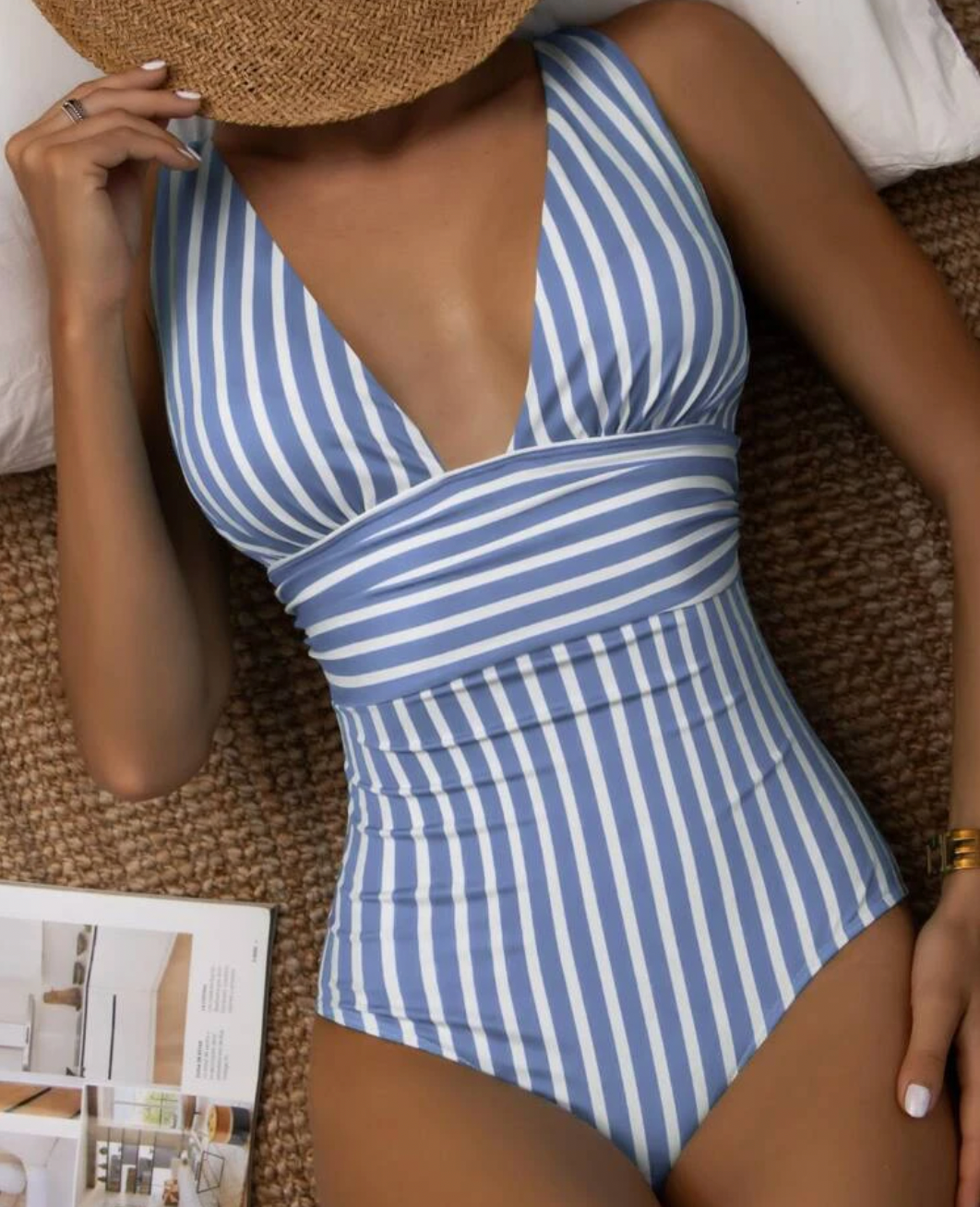 Costume intero a righe blu e bianche, scollo a V, indossato da una donna con cappello di paglia. Moda mare estiva, stile elegante.