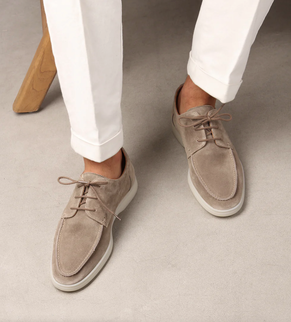 Scarpe da uomo in camoscio beige, eleganti e casual, abbinate a pantaloni bianchi. Scarpe stringate con suola bianca, ideali per look estivi.
