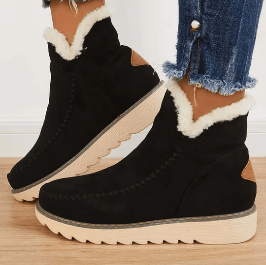 Stivaletti neri invernali da donna con fodera in pelliccia sintetica, suola in gomma beige, dettagli marroni, abbinati a jeans strappati.