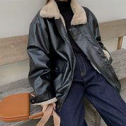 Giacca in pelle nera con colletto in pelliccia sintetica, abbinata a jeans blu e maglione nero. Moda autunnale, stile casual chic.
