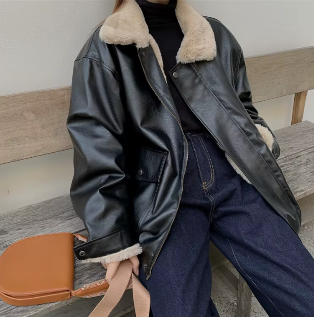 Giacca in pelle nera con colletto in pelliccia sintetica, abbinata a jeans blu e maglione nero. Moda autunnale, stile casual chic.