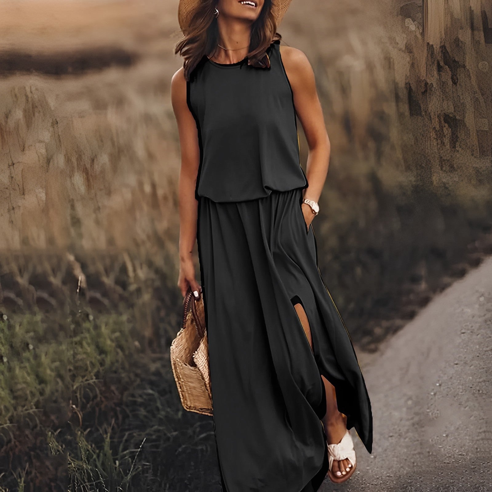 Abito lungo nero estivo donna, senza maniche, con spacchi laterali. Accessori: cappello di paglia, borsa intrecciata. Look casual elegante.