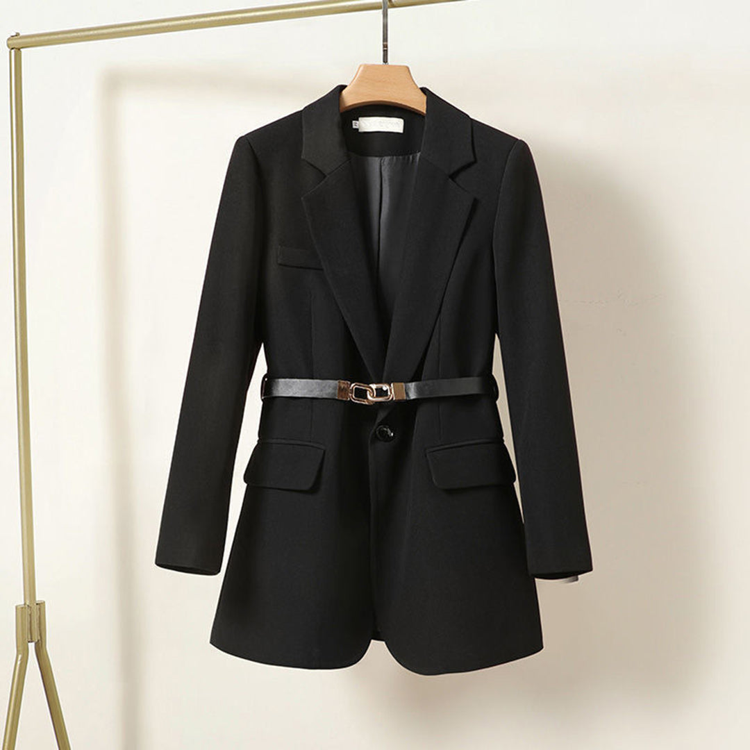 Giacca blazer nero da donna con cintura, elegante e moderna, appesa su appendiabiti. Ideale per abbigliamento formale e casual.