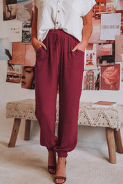 Donna in pantaloni jogger bordeaux, camicia bianca, sandali marroni. Sfondo con collage di foto. Moda casual, abbigliamento estivo donna.