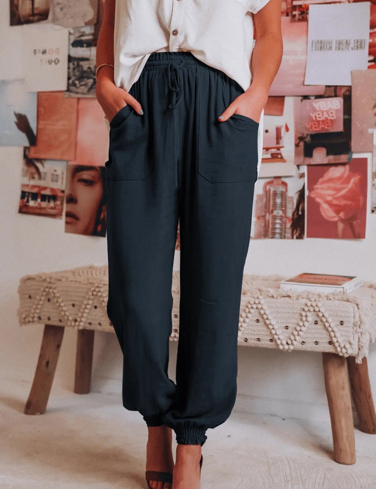 Donna in pantaloni neri larghi e camicia bianca, posa in un ambiente moderno con poster artistici. Moda casual, abbigliamento femminile elegante.