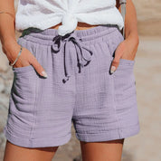 Shorts donna in cotone viola chiaro, con tasche e laccio in vita, indossati con top bianco annodato. Stile casual estivo, moda femminile.
