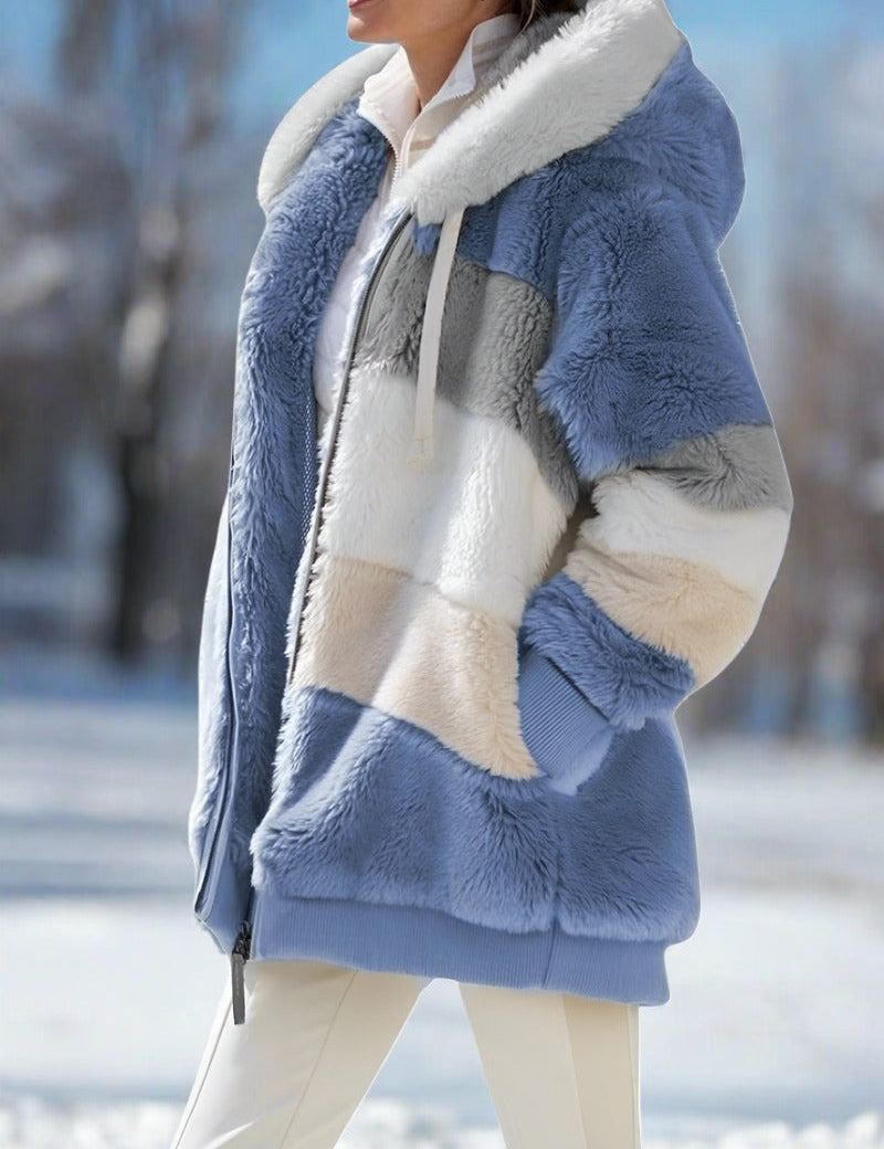 Giacca invernale donna in pelliccia sintetica a blocchi di colore blu, bianco e grigio, con cappuccio, all'aperto su sfondo innevato.