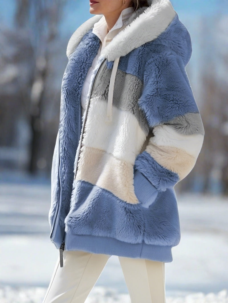 Giacca invernale donna in pelliccia sintetica a blocchi di colore blu, bianco e grigio, con cappuccio, all'aperto su sfondo innevato.