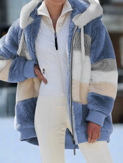 Giacca invernale donna in pelliccia sintetica a righe blu, grigie e beige, con cappuccio. Moda inverno, abbigliamento caldo e trendy.