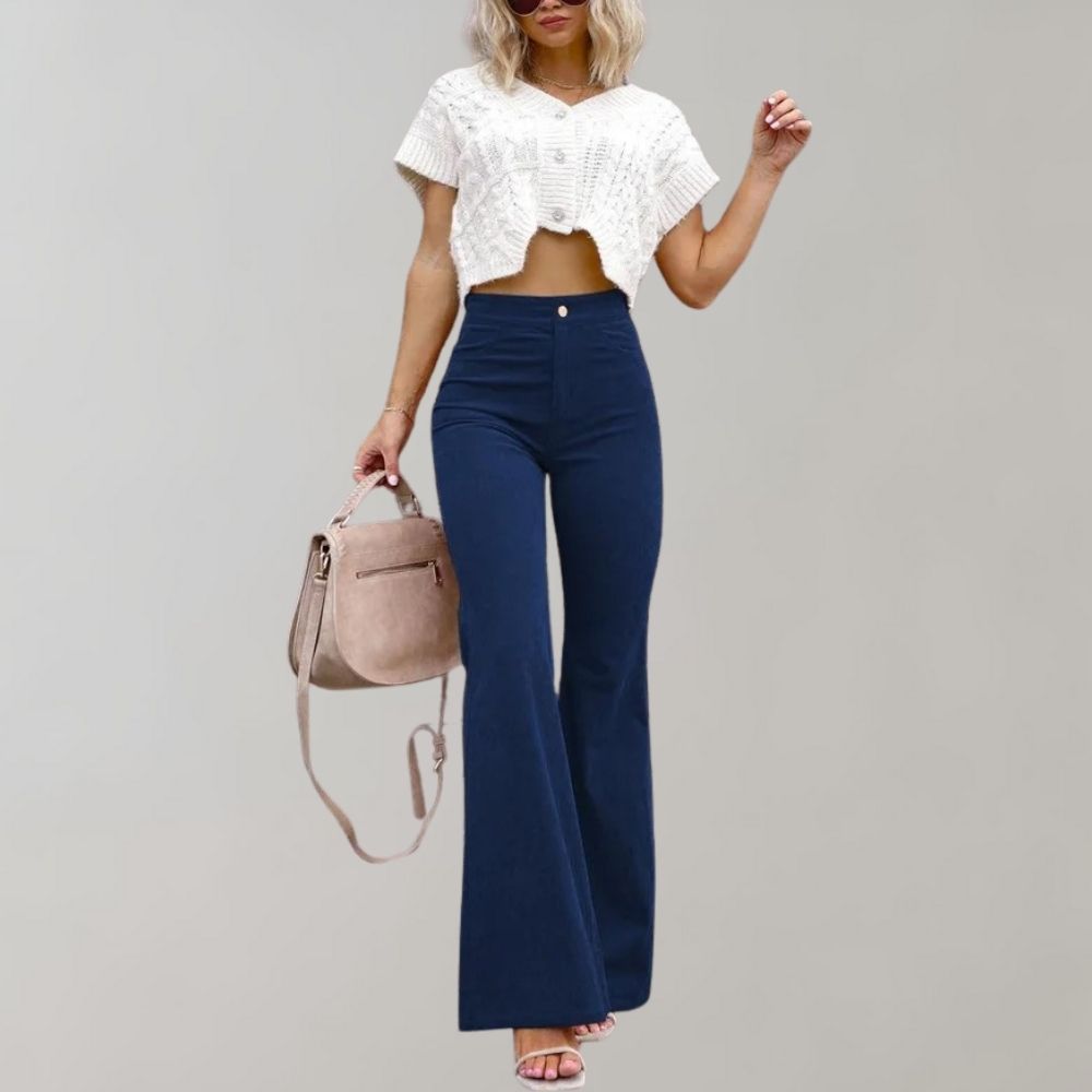 Donna con top bianco a maglia corta, pantaloni a zampa blu scuro, borsa a tracolla beige, sandali rosa. Moda casual elegante.