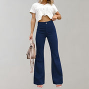 Donna con top bianco corto e pantaloni a zampa blu, borsa beige. Moda casual, abbigliamento estivo, stile trendy.