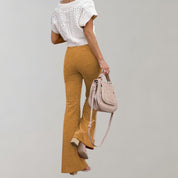Donna con pantaloni a zampa color senape, maglia bianca lavorata a maglia, borsa a tracolla beige. Moda autunnale elegante e casual.