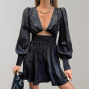 Abito nero elegante con maniche a sbuffo, scollo a V profondo e dettaglio cut-out, indossato con collana dorata e borsa nera. Moda donna chic.