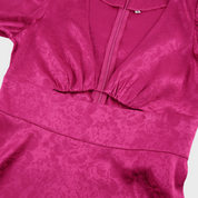 Abito rosa fucsia in raso con scollo a V profondo e dettagli floreali. Elegante e alla moda, perfetto per eventi serali o cerimonie.