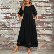 Abito lungo nero elegante con maniche trasparenti, indossato da una donna davanti a un muro di mattoni. Perfetto per eventi serali e moda estiva.