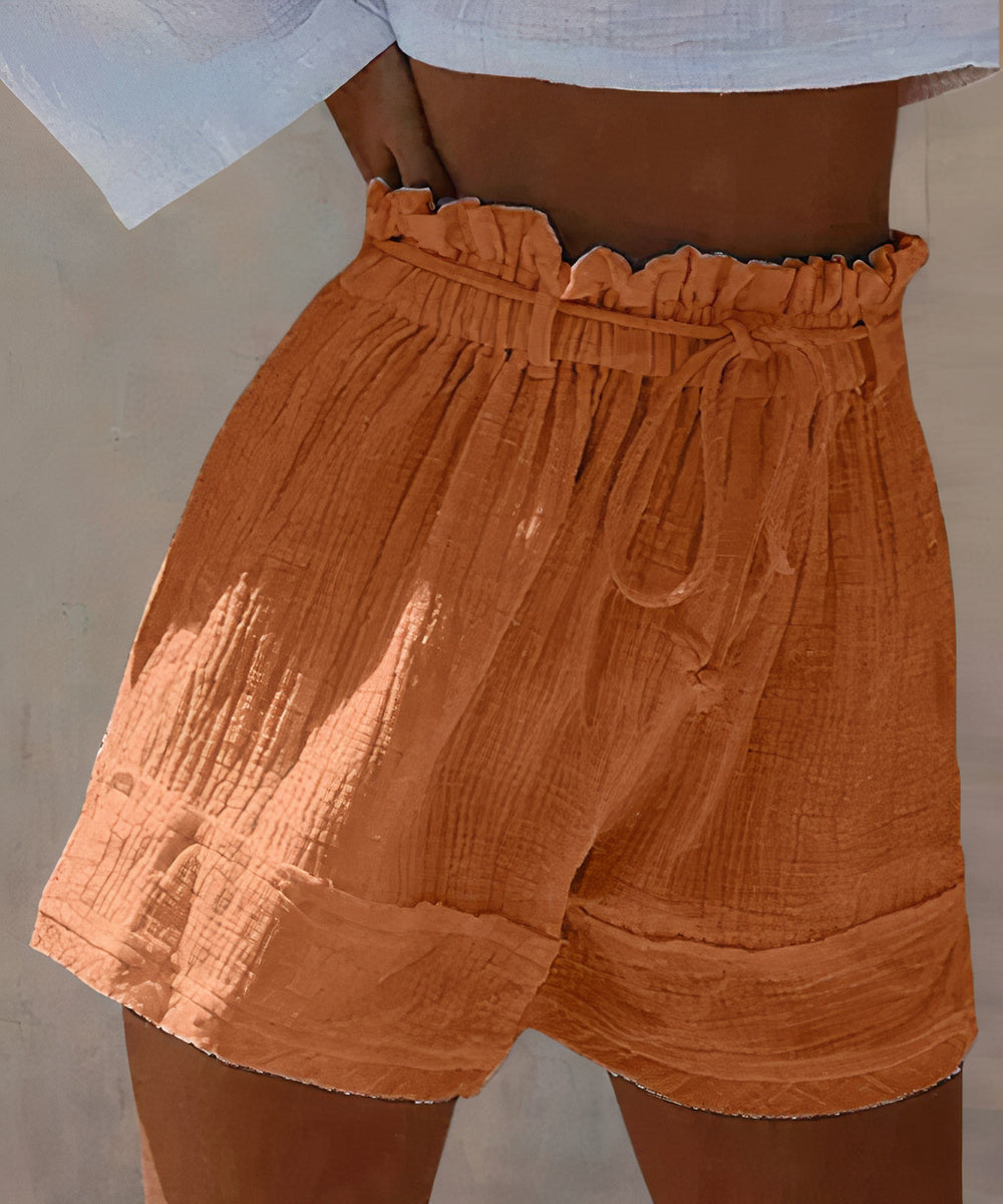 Shorts a vita alta in cotone arricciato color terracotta, con cintura regolabile. Moda estiva donna, abbigliamento casual, tendenza 2023.