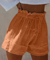 Shorts a vita alta in cotone arricciato color terracotta, con cintura regolabile. Moda estiva donna, abbigliamento casual, tendenza 2023.