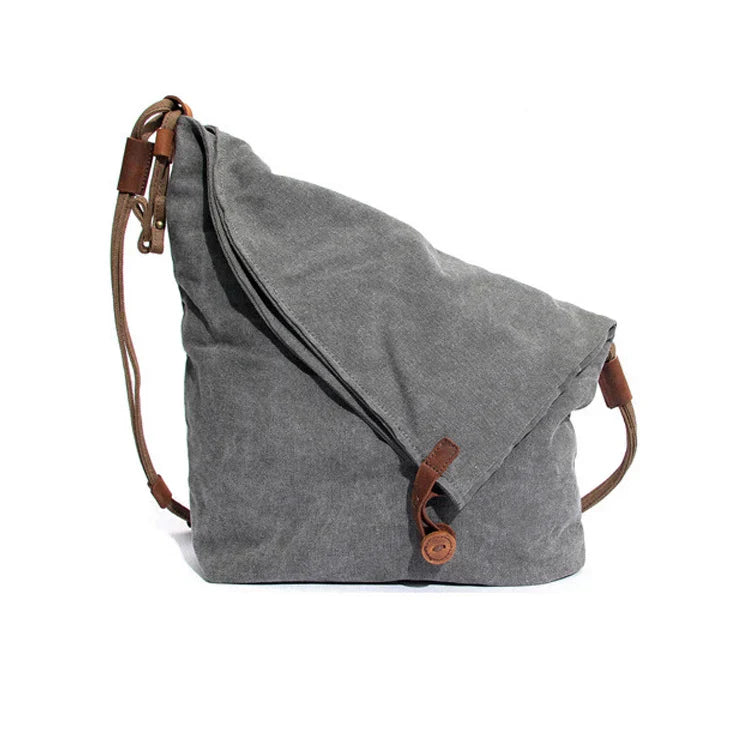 Zaino a tracolla in tela grigia con dettagli in pelle marrone, design casual e spazioso, ideale per viaggi e uso quotidiano.
