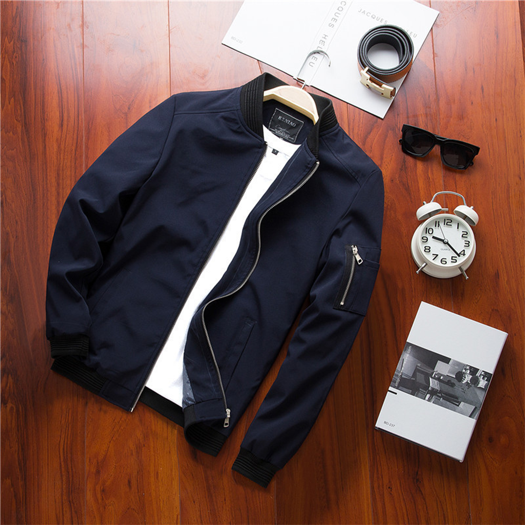 Giacca bomber blu scuro da uomo su sfondo in legno, con zip, accanto a orologio, occhiali da sole e scatola. Stile casual elegante.