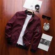 Giacca bomber bordeaux su sfondo in legno, con zip aperta, maglietta bianca, orologio, occhiali da sole e sveglia. Moda uomo casual elegante.