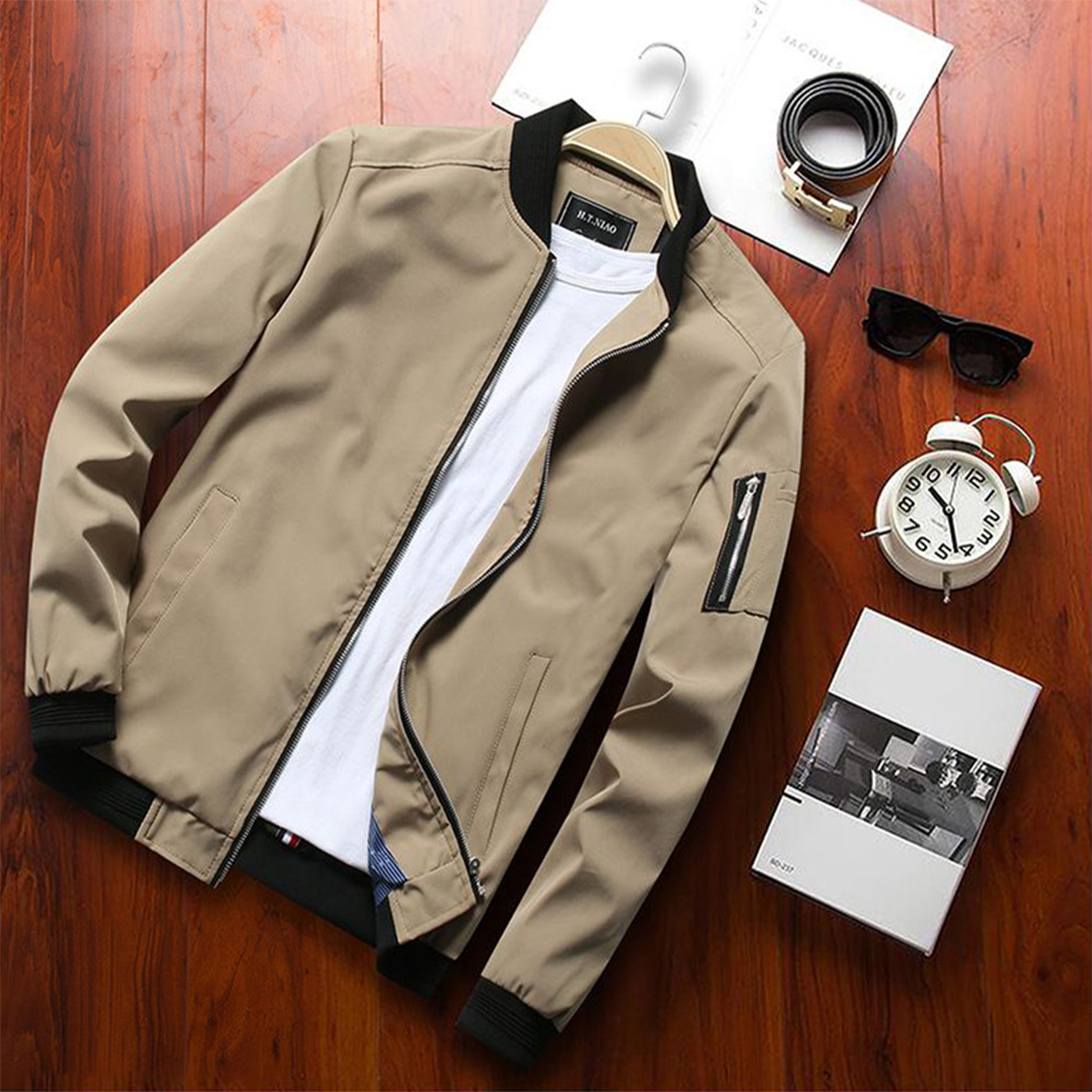 Giacca bomber beige da uomo su tavolo in legno, con t-shirt bianca, orologio, occhiali da sole e scatola. Moda casual, abbigliamento maschile.