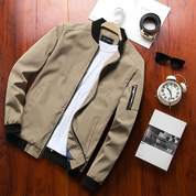 Giacca bomber beige da uomo su tavolo in legno, con t-shirt bianca, orologio, occhiali da sole e scatola. Moda casual, abbigliamento maschile.