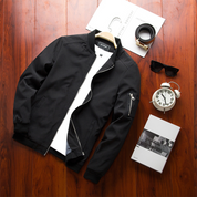 Giacca bomber nera da uomo su sfondo in legno, con zip, occhiali da sole, orologio sveglia e scatola regalo. Moda casual, abbigliamento maschile.