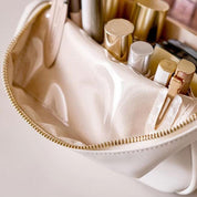 Astuccio cosmetico beige aperto con cerniera dorata, contenente rossetti, pennelli e accessori trucco. Elegante e pratico per organizzare il make-up.