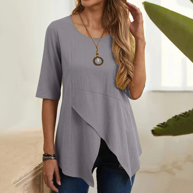 Blusa grigia da donna con maniche a tre quarti, design asimmetrico, collana pendente, abbinata a jeans. Moda casual elegante per ogni occasione.