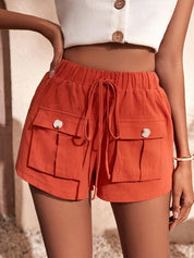 Shorts arancioni da donna con tasche frontali e laccetti, abbinati a un top bianco. Stile estivo casual, moda femminile, abbigliamento leggero.