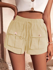 Shorts estivi beige da donna con tasche frontali e coulisse, abbinati a top bianco senza maniche. Look casual e alla moda per l'estate.