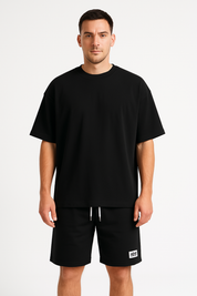 Maglietta nera oversize uomo, abbinata a pantaloncini neri con logo bianco. Abbigliamento casual, moda uomo, stile minimalista.