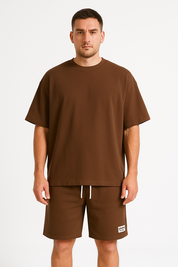 Uomo in t-shirt marrone e pantaloncini abbinati, stile casual. Abbigliamento estivo, moda uomo, outfit comodo. Sfondo bianco.