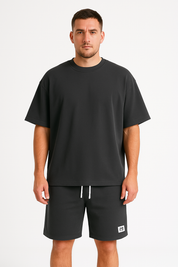 Uomo in t-shirt nera oversize e pantaloncini abbinati, su sfondo bianco. Abbigliamento casual, moda uomo, stile minimalista.