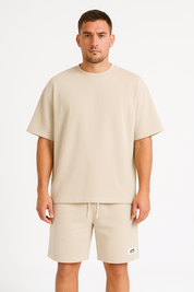 Uomo in t-shirt beige oversize e pantaloncini abbinati, moda casual estiva, abbigliamento uomo, sfondo bianco.