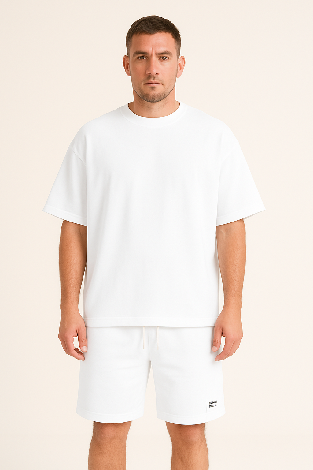 Uomo in t-shirt bianca oversize e pantaloncini abbinati, moda casual estiva, abbigliamento maschile minimalista, sfondo neutro.