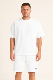 Uomo in t-shirt bianca oversize e pantaloncini abbinati, moda casual estiva, abbigliamento maschile minimalista, sfondo neutro.